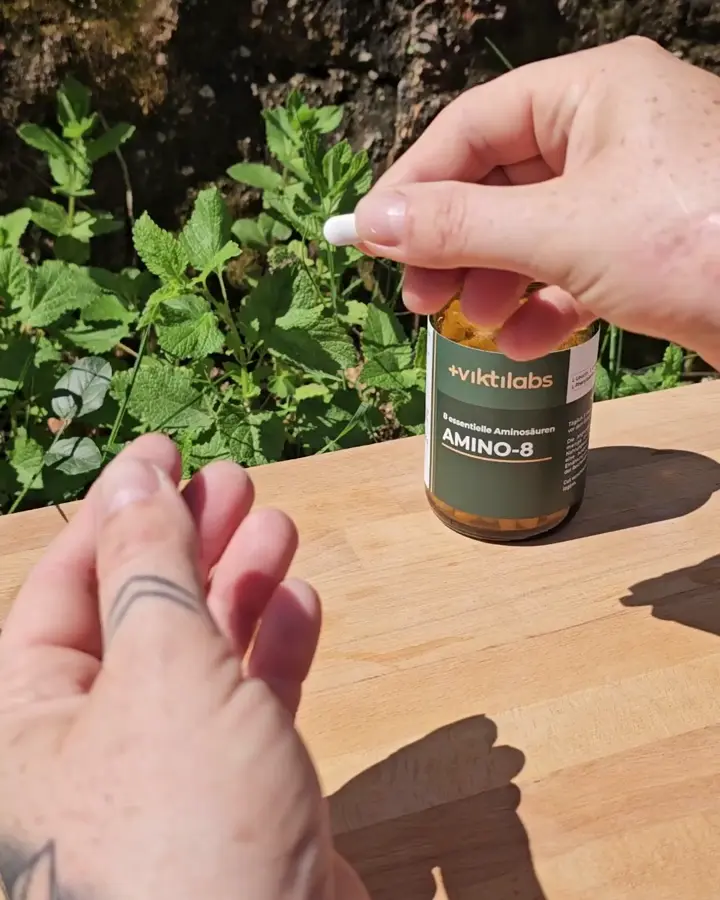 Ein Pressling zwischen zwei Fingern, das Glas Amino-8 im Hintergrund