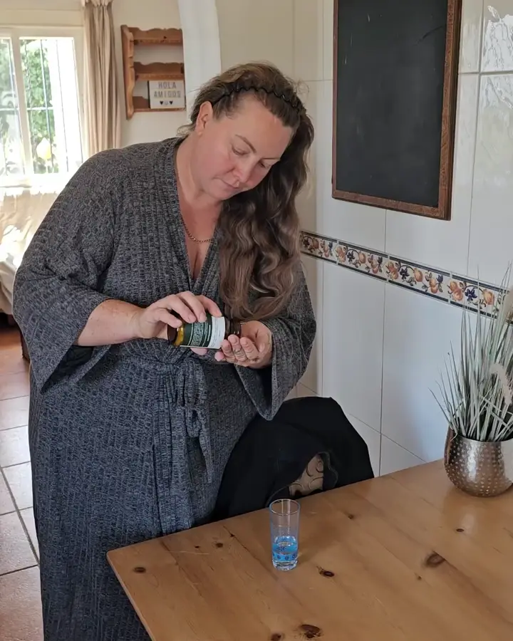 Frau schüttet sich am Küchentisch ihre Presslinge in die Hand, ein Glas Wasser steht bereit